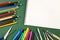 Colorful pencils, scissor, felt tip markers, paint brushes and blank sketchbook sheet with copy space on dark green background. Ba