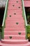 Colorful pink stair with green wooden handrails outdoors