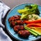 A colorful platter of assorted vegetables, marinated meat and cooked rice is on a wooden table