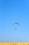 Colorful powered parachute against blue sky and yellow field.