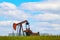 Colorful pump jack on oil well - low horizon on prairie with green grass and wild flowers - big blue cloudy sky - room for text