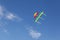 Colorful rainbow kite hovers in the air high in the sky. Blue sky with clouds. Copy space