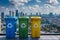 Colorful recycling bins against a cityscape background.