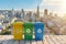 Colorful recycling bins against a cityscape background.