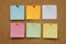 Colorful reminder sticky notes push pins on cork board.