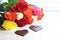 Colorful roses with chocolate hearts on white wooden boards