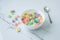 Colorful round cereals filled with milk in a white plate. Balls scattered on a white table. Cooking breakfast