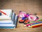 Colorful school supplies with books, color pencils, pink glasses, pen and cutter on wooden background.