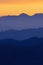 Colorful silhouettes of layers of hills with bright orange sky in background