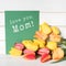 Colorful Spring Tulips in red and Yellow with a green card with love you, Mom wishes stamped on it. Square with white shiplap boar