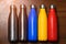 Colorful stainless thermo bottles, on a wooden table sprayed with water. Matte red bottle, blue, yellow and platinum color. With s