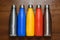 Colorful stainless thermos bottles on a wooden table sprayed with water.