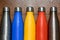 Colorful stainless thermos bottles on a wooden table sprayed with water.