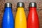 Colorful stainless thermos bottles on a wooden table sprayed with water.