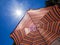 Colorful striped parasol against the sky and the sun. Hot weather. A beach holiday