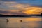 Colorful sunset as seen from the Morro Bay harbor; silhouettes of people enjoying the view from the kayak and paddle board;