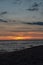 colorful sunset over calm sea beach with dark blue water and dramatic contrasty clouds