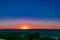 A colorful sunset over a clear sky of unusual color, around uneven large and spacious fields with green vegetation