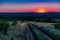 A colorful sunset over a clear sky of unusual color, around uneven large and spacious fields with green vegetation