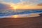 Colorful sunset at the tropical beach, sun behind clouds reflects on water.