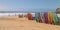 Colorful surfboards lined up on a sandy beach, with a group of people preparing for a family surfing lesson in the