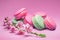 Colorful sweet macarons or macaroons, cherry flavored cookies on pink background with blooming cherry branch near them