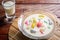 Colorful sweet rice gnocchi in fresh coconut milk in glass bowl on brown tablecloth on blackground. Delicious Thai desserts