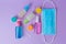 Colorful travel size bottles and medical masks on lavender background.