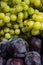 Colorful variety of waxy fruits on counter of farmer`s market grapes, plums