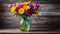 A colorful vase filled to the brim with fresh flowers perched atop a rustic wooden table displays a burst of blooms.