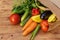 Colorful vegetables in a paper bag lying on their side on a brown wooden board, side view from above