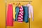 Colorful womens clothes on hangers on rack on orange background.