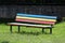 Colorful wooden boards public bench with faded color and metal support frame surrounded with uncut grass at local public park