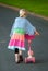 Colorfully dressed young girl pushes pink scooter away from camera