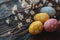 Colorfully painted Easter eggs with flowers on branches rest on dark wood. This image is steeped in the festive spirit