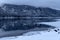 Colorless winter lake with snow ice and a dark forest