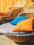 Colourful pillows on modern daybed. Brown rattan loungers with orange and blue pillows hanging with rope by relaxing terrace.