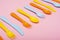 Colourful plastic tableware : forks, knifes and spoons on pink background in row