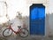 Colourful summer scene of an old red bike outside a greek house with whitewashed walls and a blue painted door in bright sunlight