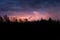 Colourful summer thunder storm over the forest at night. Spectacular lighting strikes in the sky