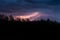 Colourful summer thunder storm over the forest at night. Spectacular lighting strikes in the sky