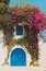 Colourful tropical purple bougainvillea creeper flowering over blue door on a whitewashed villa