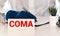 Coma - word from wooden blocks with letters holding by a doctor's hands in medical protective gloves