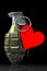 A combat grenade with a red heart hanging on a ring. The concept of strong feelings and love. Black background. Valentine`s Day
