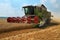 Combine harvester working on a golden ripe wheat field on a bright summer day against blue sky with clouds. Grain dust in the air