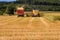 Combines harvesting grains and filling tractor trailer in summer on field