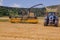 Combines harvesting grains and filling tractor trailer in summer on field