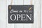 Come in we`re Open text on a hanging chalkboard on weathered whitewash textured wood