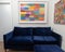 Comfortable blue velvet sofa with matching blue velvet footstool and colourful framed artwork on the walls.