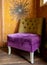 Comfortable chair in corner of living room, upholstered in purple and mustard colour velvet fabrics.